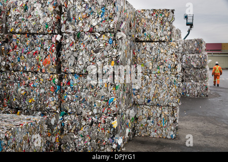 Un trabajador camina pasado montones de cubos de latas de metal aplastado que aguardan el envío a una planta de reciclaje que poseen. Foto de stock