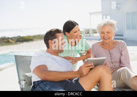 Familia usando tableta digital al lado de la piscina Foto de stock
