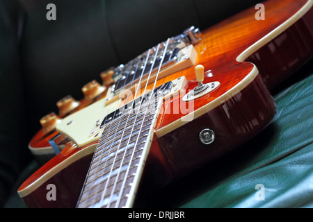 Guitarra eléctrica LP forma elegante, cuerpo de caoba, arce rojo arriba en un sofá de cuero. DOF superficial. Foto de stock