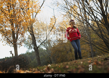 El follaje de otoño en los árboles en una granja, una joven en un puente de tejido de color rojo con un cálido tartan woolly hat