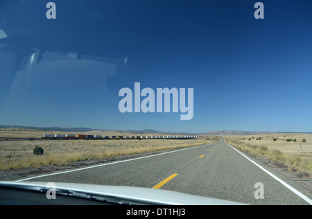 La ruta 66, Arizona, EE.UU. Larga, solitaria y de carretera recta y un enorme tren de mercancías desaparece en la distancia a través del parabrisas Foto de stock
