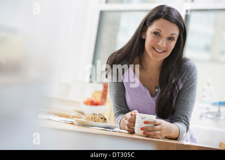 Una oficina o un apartamento interior en la Ciudad de Nueva York, una joven mujer con largo cabello negro con una taza de café