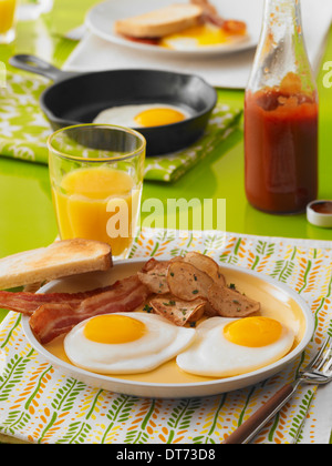 Una escena de desayuno con sunny side up huevos fritos, bacon, tostadas, patatas, desayuno y un vaso de jugo de naranja