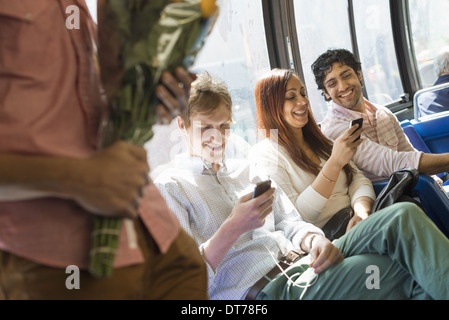 Hombres y mujeres en un autobús de la ciudad, en la ciudad de Nueva York. Dos personas controlar sus teléfonos flores. Foto de stock