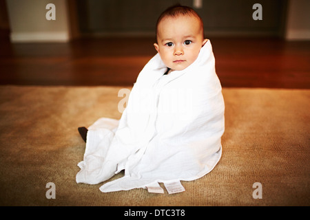 Retrato de niño envuelto en una manta sentado en el suelo