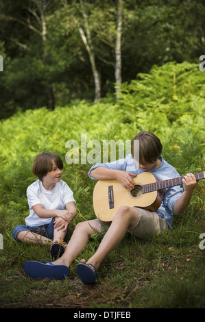 Dos muchachos camping en nuevo bosque sentado en el pasto uno tocando una guitarra Hampshire Inglaterra