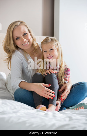 Retrato de feliz madre e hija sentada en la cama en casa