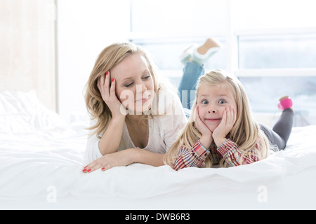 Madre mirando hermosa hija haciendo caras mientras está acostada en la cama
