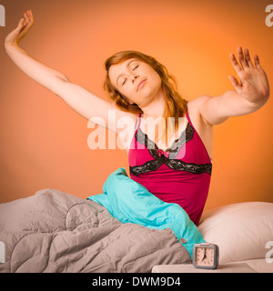 Bastante mujer estirando los brazos tras despertarse temprano en las mañanas en el acogedor dormitorio