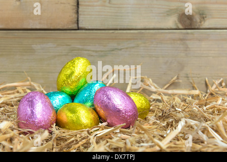 Lámina de chocolate cubierto de huevos de Pascua en un nido de paja en un granero Foto de stock