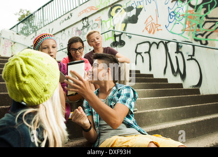 Un grupo de niños sentados en las escaleras exteriores, utilizando ordenadores Tablet y smartphones, Alemania Foto de stock