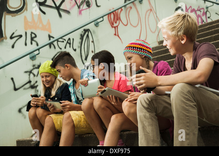 Un grupo de niños sentados en las escaleras exteriores, utilizando ordenadores Tablet y smartphones, Alemania Foto de stock