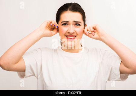 Una joven mujer caucásica slim atractiva chica, en un entorno ruidoso, sufriendo dolor de oído con los dedos en sus orejas UK Foto de stock