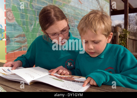 Los alumnos de la escuela primaria (años 2 & 6) lectura en el patio de recreo, Farnham, Surrey, Reino Unido.