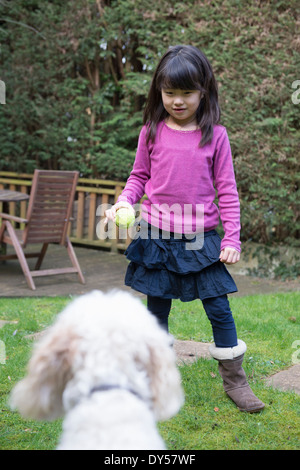 Chica jugando a la pelota con su perro en el jardín