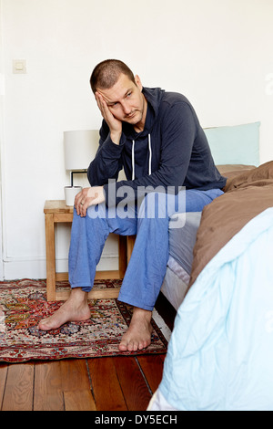 Mitad hombre adulto infeliz sentada en la cama con la cabeza en la mano Foto de stock