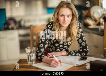 Una chica de 16 años realizando tareas de matemáticas sobre la mesa de la cocina. Foto de stock
