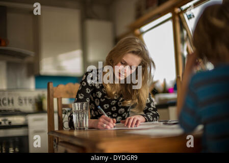 Una chica de 16 años realizando tareas de matemáticas sobre la mesa de la cocina. Foto de stock