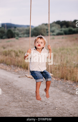 Niño feliz jugando en el columpio en un parque Foto de stock