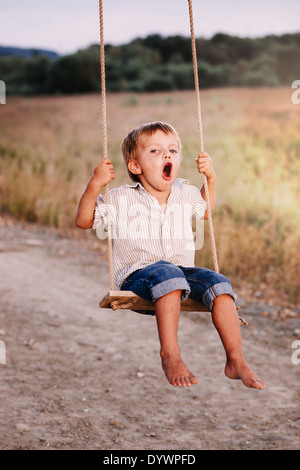 Niño feliz jugando en el columpio en un parque Foto de stock