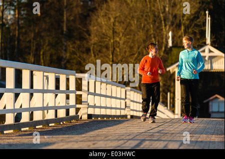 Dos mujeres correr juntos a lo largo del puente al amanecer. Foto de stock
