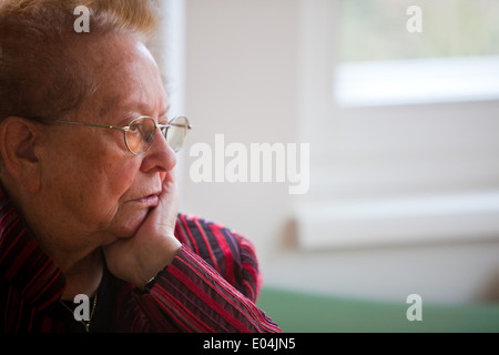 En la vieja mujer sentada pensativamente en la ventana, Eine alte Frau sitzt nachdenklich am Fenster Foto de stock