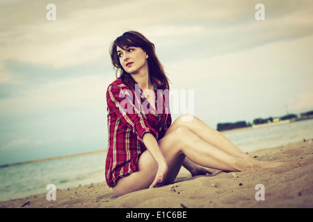 Mujer joven en un rojo de camisa de cuadros para relajarse en la playa en el atardecer. Foto de stock