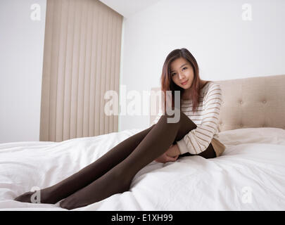 Longitud total retrato de hermosa mujer joven en medias sentada en la cama Foto de stock
