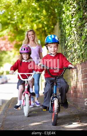 Los niños andando en bicicleta en su camino a la escuela con la madre Foto de stock
