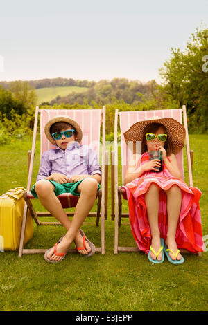 Chico y chica luciendo sombrero de paja y gafas de sol sentados en sillas de cubierta