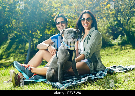 Retrato de pareja y perro sentado en manta para picnic en el parque