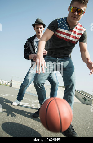 Los hombres jóvenes jugando baloncesto en skatepark Foto de stock