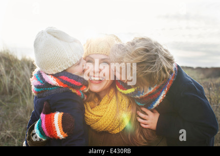 Mitad mujer adulta con hijo e hija besar su mejilla en la costa