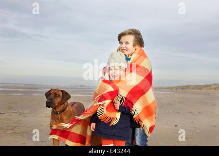 Retrato de niña de tres años y el hermano envuelto en manta en la playa, Bloemendaal aan Zee, Holanda