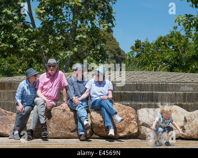 Los abuelos sentados en el parque y nieto chapoteando en el agua