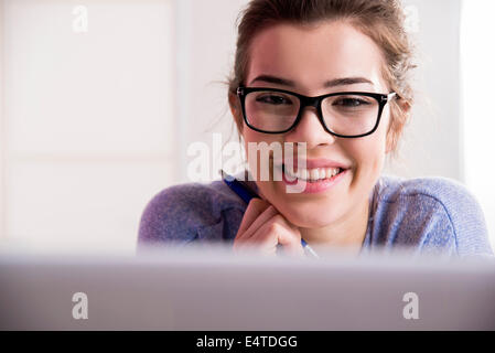Close-up retrato de mujer joven con ordenador portátil usando gafas, sonriendo y mirando a la cámara, Foto de estudio