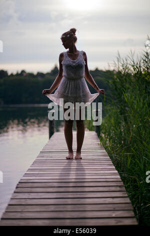 Mujer joven en vestido blanco permanente de una pasarela sobre el lago Foto de stock