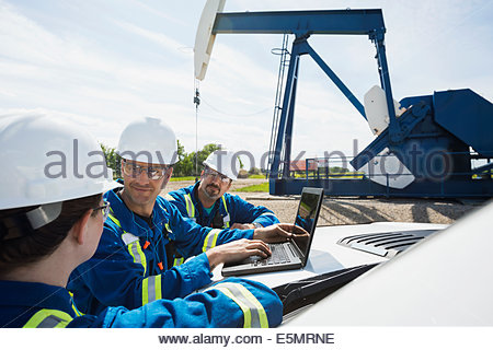 Los trabajadores con portátil hablando cerca del pozo de petróleo