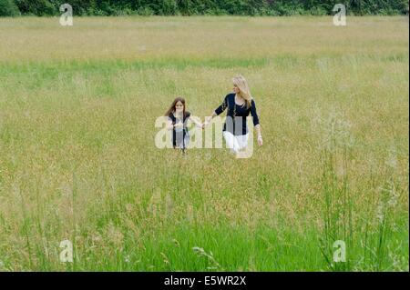 Madre e hija paseando por campo de hierba larga Foto de stock