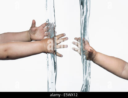Vista compuesta de niños pequeños brazos y manos llegando desde lados opuestos en agua clara Foto de stock