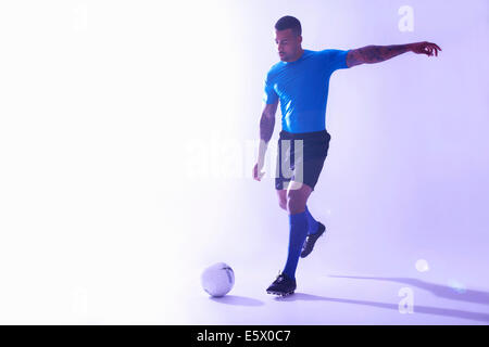 Foto de estudio de macho joven futbolista pateando la pelota