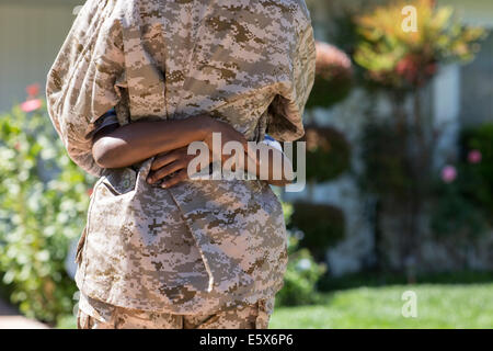 Vista trasera recortada de mujer soldado abrazando a hijo en casa Foto de stock