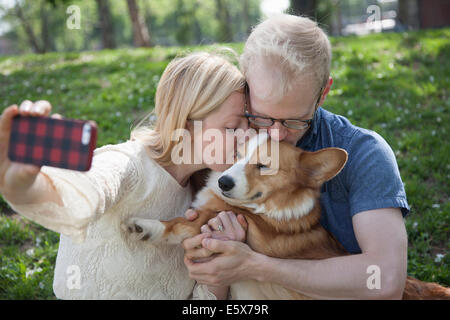 Pareja joven en el parque tomando selfie mientras besa corgi perro