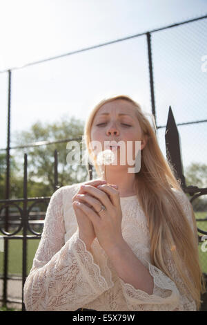 Mujer joven con ojos cerrados soplando jaramago reloj en park