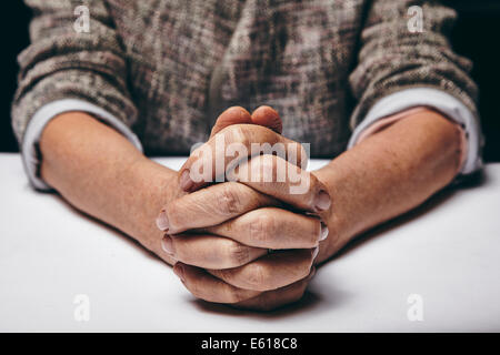 Fotografía de estudio de rezar las manos de una mujer mayor en la tabla. Viejo las manos entrelazadas en una tabla. Foto de stock