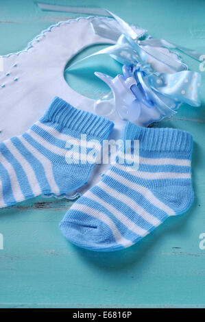 Baby Boy vivero calcetines blancos y azules, y babero chupete, en aqua vintage shabby chic antecedentes Foto de stock