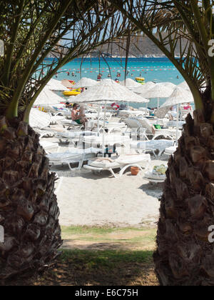 Cesme, Turquía, Agosto 2nd, 2014: playa turística en la península Cesme en temporada alta son vistos a través de las palmeras. Foto de stock