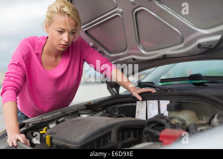 Mujer de inspeccionar el motor del coche roto.