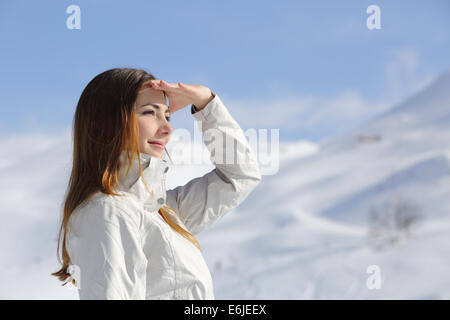 Caminante mujer mirando hacia la montaña nevada con su mano sobre la frente Foto de stock