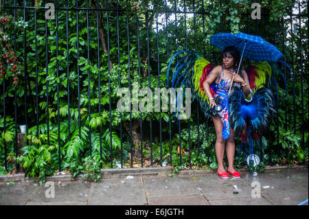 Londres, Reino Unido. 25 Aug, 2014. Un juerguista en un traje protege de la lluvia bajo un paraguas azul durante el carnaval de Notting Hill en Londres. Crédito: Piero Cruciatti/Alamy Live News Foto de stock
